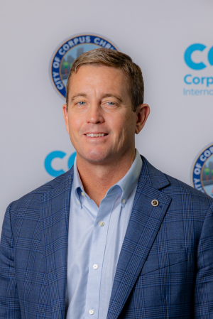 Professional headshot of Travis Patterson against an Airport logo background, smiling.