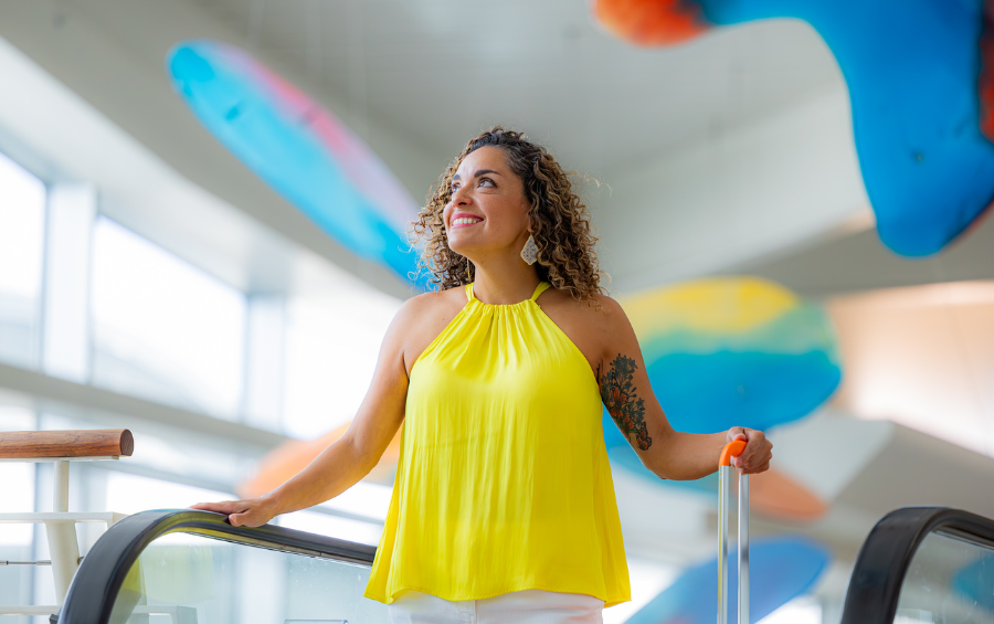 Middle-aged woman in a bright yellow shirt, on an escalator at Corpus Christi International Airport.
