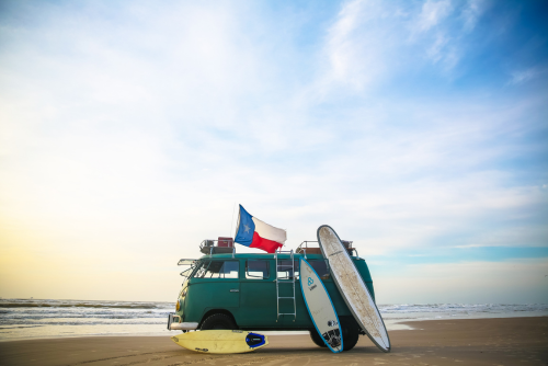 Vintage van with surfboards on a sandy beach under blue sky promoting adventure and coastal exploration
