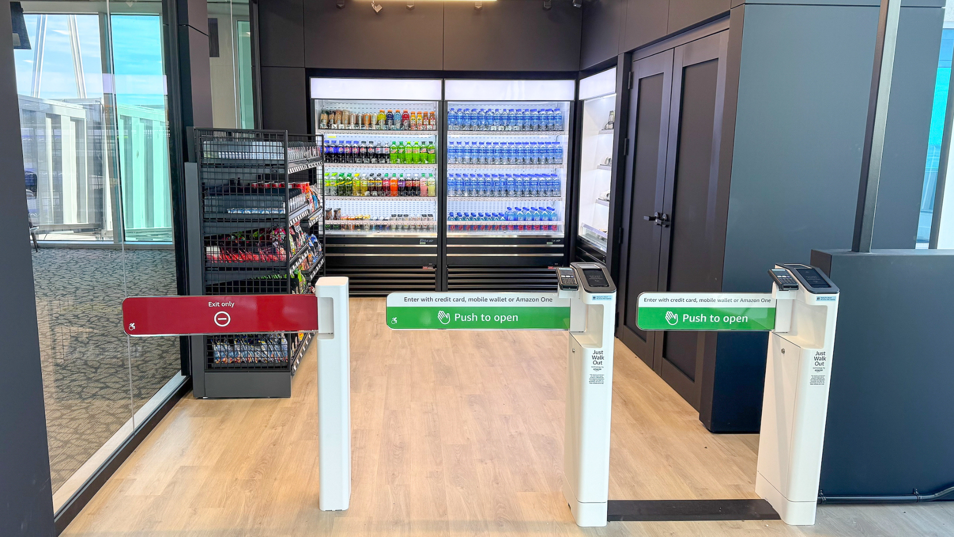 Modern convenience store entrance with payment options sign and shelves stocked with snacks and drinks.